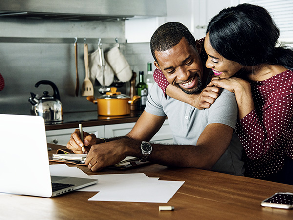 Man and woman sitting in kitchen embracing fondly while reviewing paperwork together. 