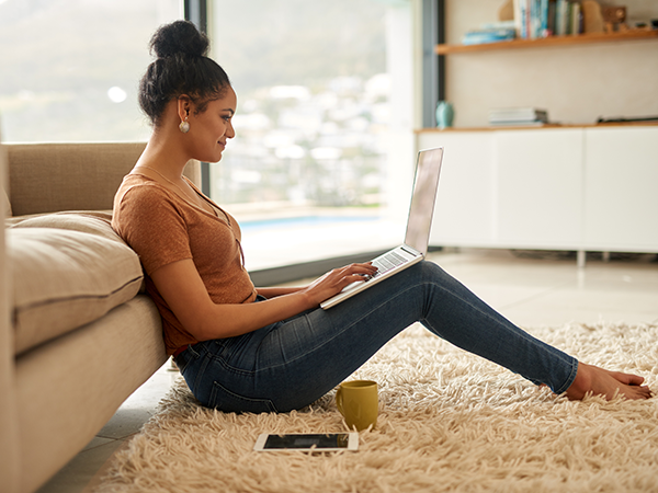 Young woman sitting in front of couch on laptop